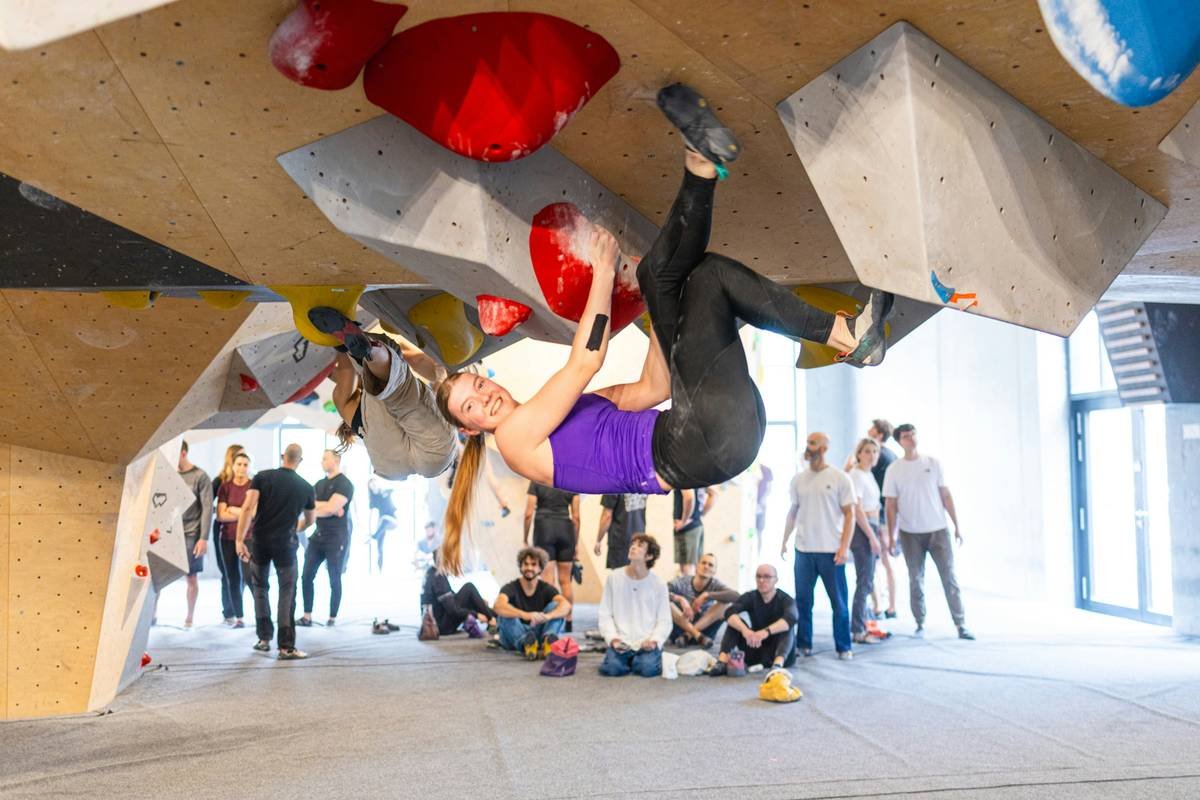 Woman mid-climb wearing dark compression tights labeled flexibility fit climbing